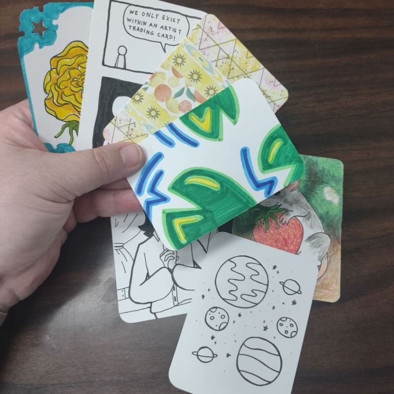 Photo of a hand holding multiple Artist Trading Cards